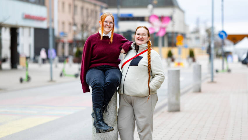 Kaksi punahiuksista henkilöä taustallaan kaupunkia.