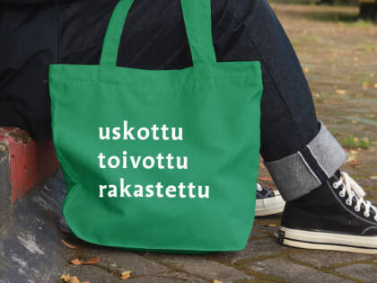Henkilö istuu jalkakäytävän reunalla vieressään kangaskassi, joka mainostaa seurakuntavaaleja.