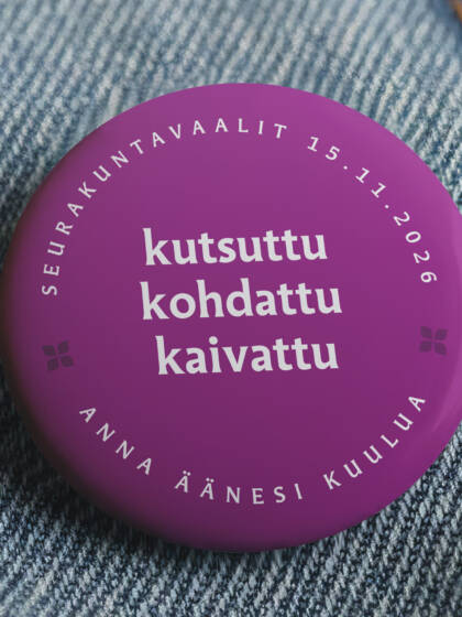 Farkkutakkiin kiinnitetty rintamerkki, joka mainostaa seurakuntavaaleja.