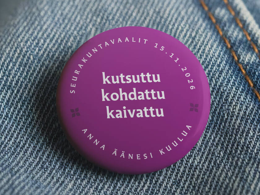 Farkkutakkiin kiinnitetty rintamerkki, joka mainostaa seurakuntavaaleja.