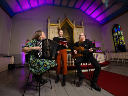 Three adults at Törnävä Church, each playing a different instrument.
