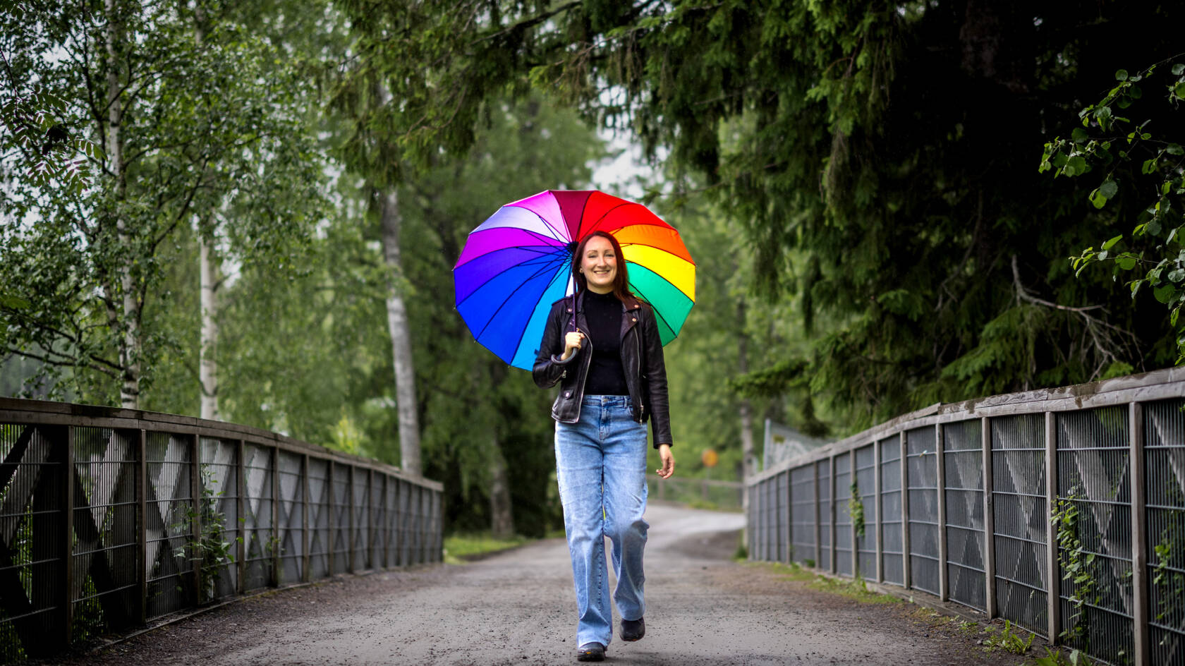 Henkilö kävelee sillalla sateenvarjon kanssa.