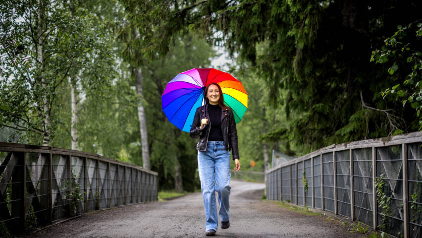 Henkilö kävelee sillalla sateenvarjon kanssa.