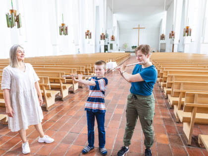 Yksi aikuinen ja kaksi lasta Lakeuden Ristin kirkkosalissa musisoimassa.