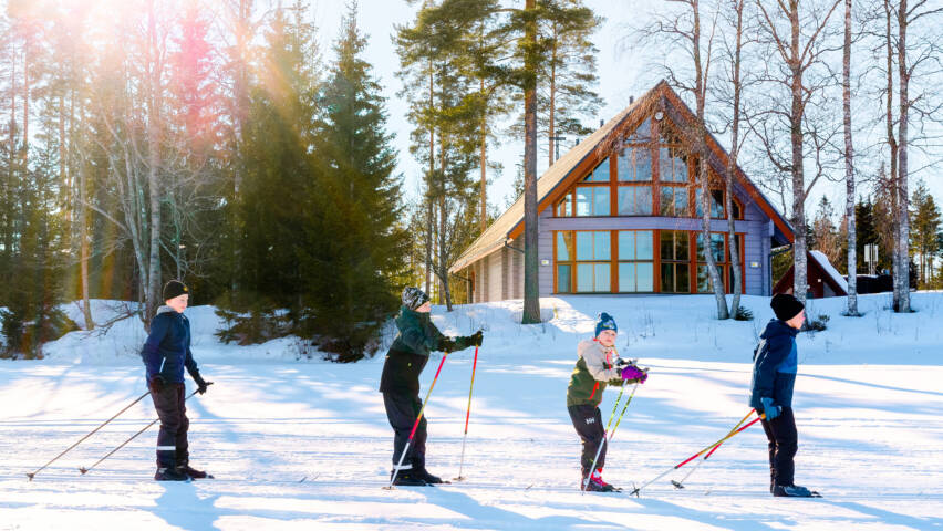 Neljä lasta hiihtää aurinkoisella säällä.