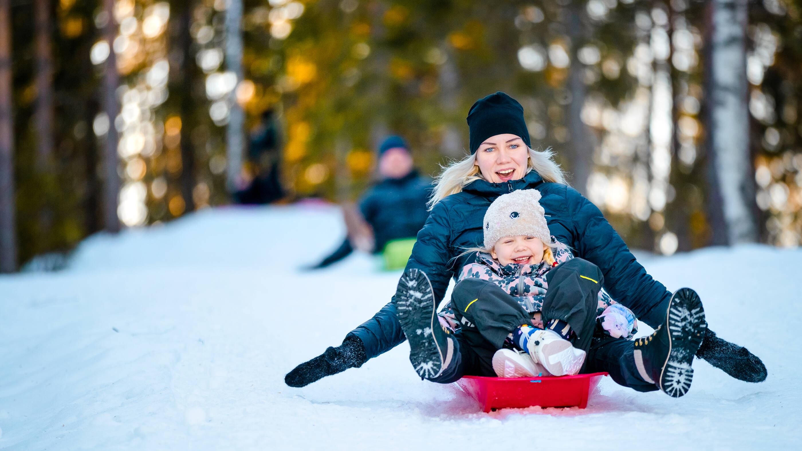 Aikuinen ja lapsi laskevat yhdessä pulkalla mäkeä.