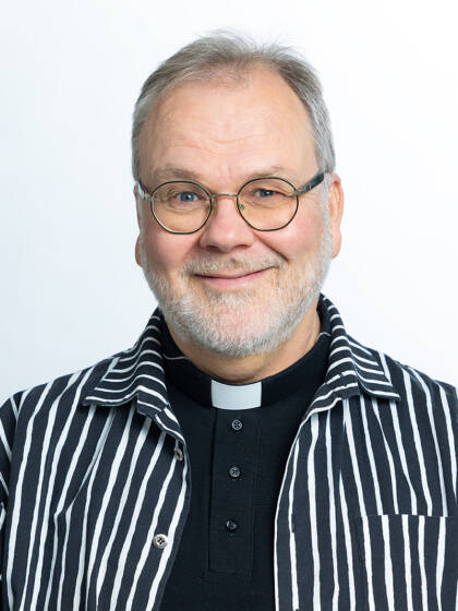 Mies ruudullisessa paidassa. Sen alla papin paita.