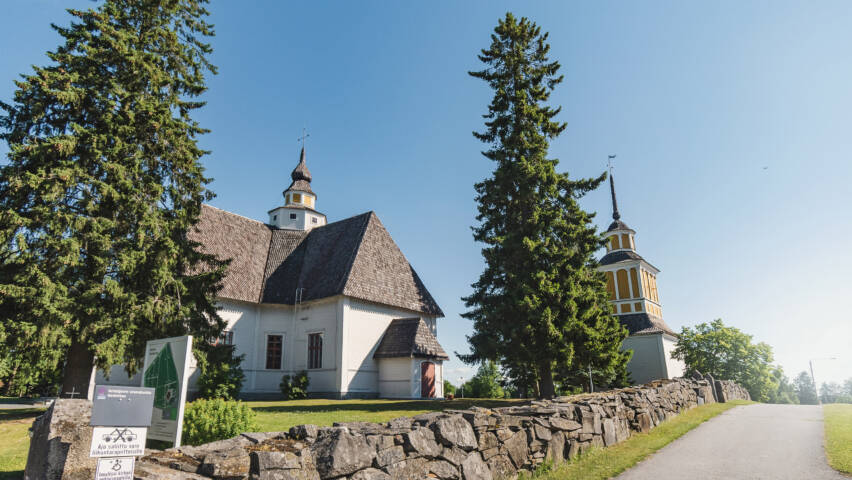Vaalea ruskeakattoinen kirkkorakennus, etualalla kiviaitaa.