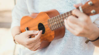 Lähikuva käsistä soittamassa ukulelea.