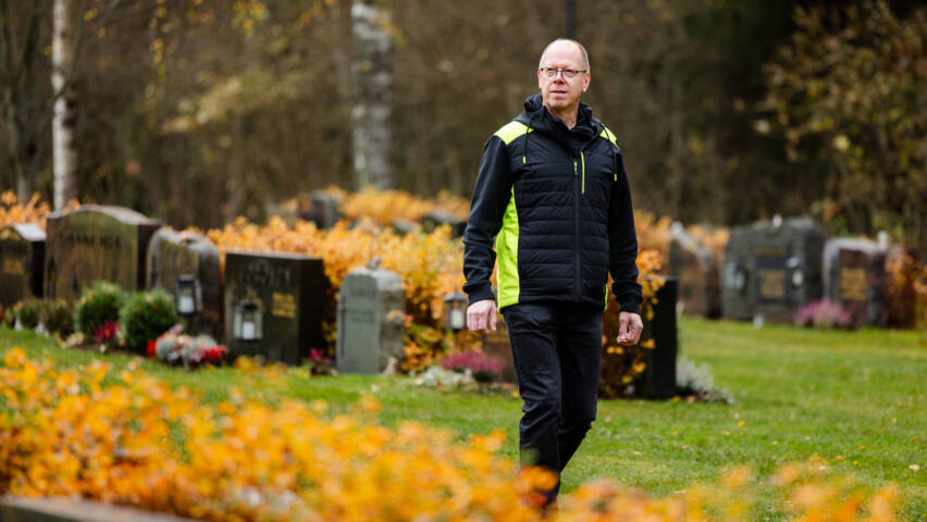 Henkilö kävelee hautausmaalla syksyisessä maisemassa.