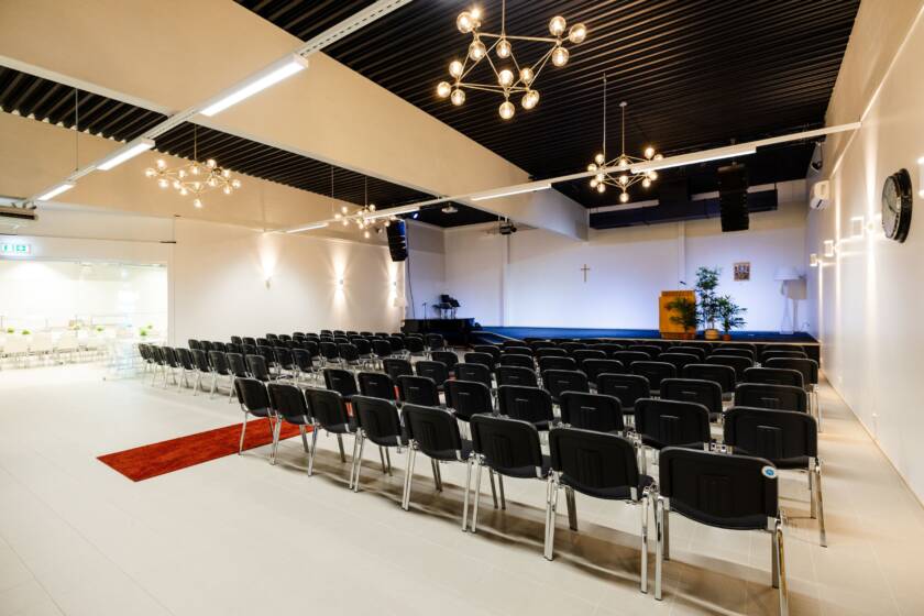 A space with a stage at the front. Black chairs and a black ceiling.